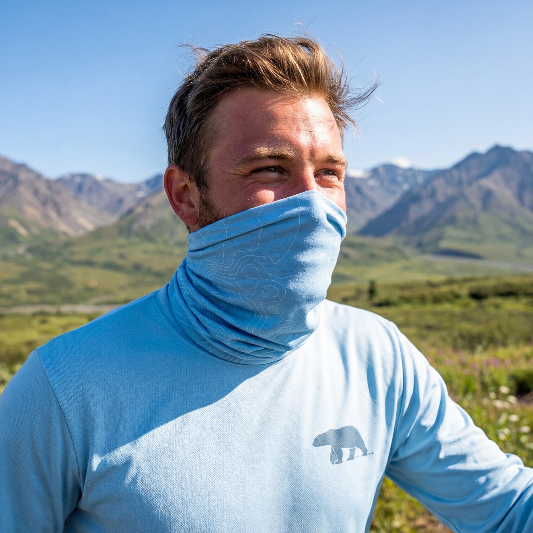Man wearing a light blue shirt and neck gaiter with mountains in the background