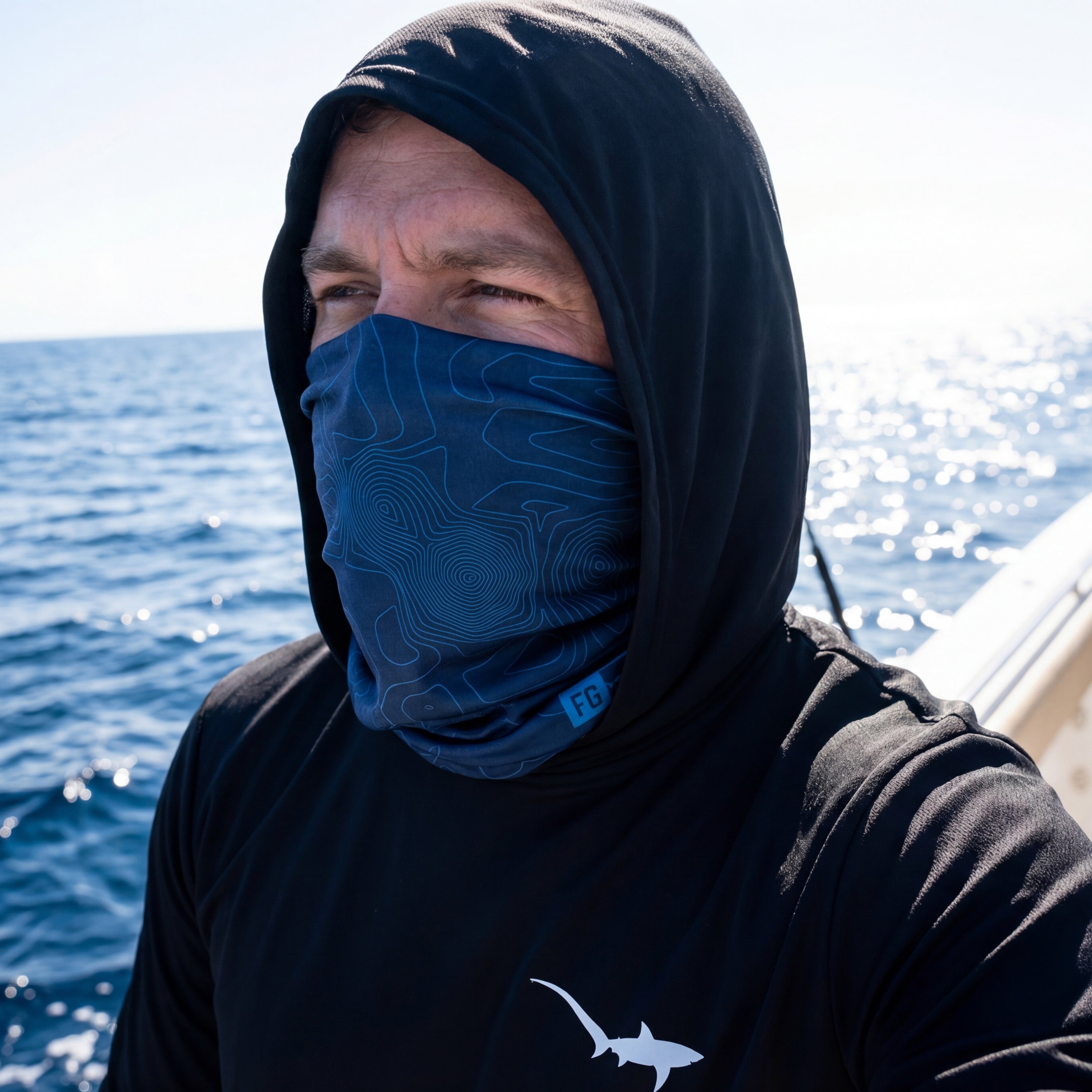 Man wearing a black hood and blue neck gaiter with ocean in the background